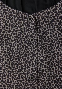 Panneau de tissu imprimé léopard avec trois boutons noirs et blancs étiquetés "Street One Studio" sur un fond noir.