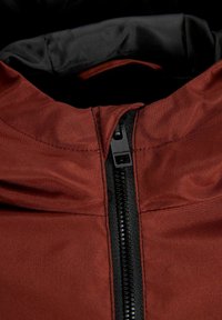 Crvena jakna s crnim patentnim zatvaračem i ovratnikom. Glatka tekstura tkanine s suptilnim sjajem. Na povlačniku patentnog zatvarača otisak "JACK & JONES."