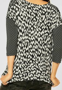 Short-sleeve top with leopard print in black and white, featuring geometric patterned sleeves and a round neckline. Soft fabric, relaxed fit.