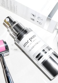 Transparent glasflaska med silverpump, märkt "ame pure Collagen Therapy." Åtföljs av en rosa microneedling-roller.