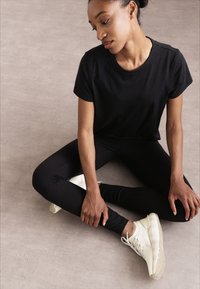 Czarna koszulka z krótkim rękawem, zestawiona z czarnymi legginsami i jasnymi trampkami, prezentująca dopasowany, wygodny fason.