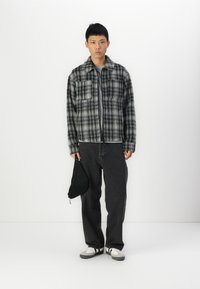 Gray and black plaid flannel jacket with two chest pockets, layered over a gray t-shirt; paired with black jeans and white sneakers.