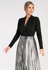 Czarna bluzka z długim rękawem w białe kropki, zestawiona z błyszcząca srebrną spódnicą plisowaną, prezentującą krój kopertowy i gładką teksturę.