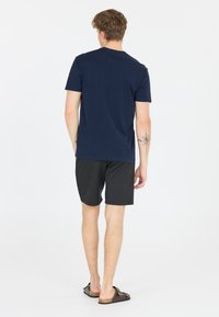 Marinblå, kortärmad t-shirt, svarta shorts, bärs med bruna rippade sandaler. Inga synliga mönster eller anmärkningsvärd hardvara. Enkel design.