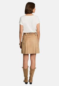 Top bianco a maniche corte abbinato a una gonna in suede beige con pieghe, una cintura con catena e stivali in suede fino al ginocchio.