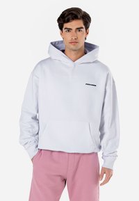 Hoodie cinza claro com um bolso frontal e o logo preto "PEGADOR". Com capuz ajustável e punhos canelados. Combinado com calças de moletom cor-de-rosa.