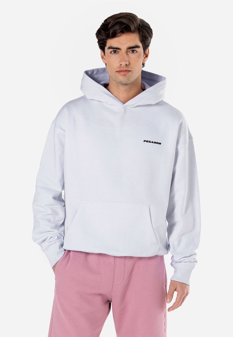 Hoodie cinza claro com um bolso frontal e o logo preto "PEGADOR". Com capuz ajustável e punhos canelados. Combinado com calças de moletom cor-de-rosa.