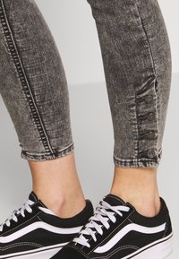 Jeans in denim grigio con un design aderente e dettagli a bottoni alle caviglie, abbinati a sneakers in bianco e nero con lacci.