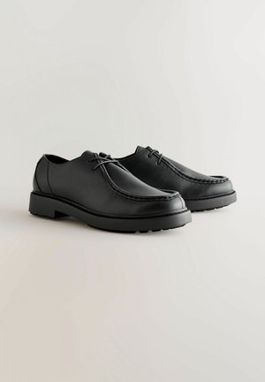 Scarpe in pelle nera con una superficie liscia, punta rotonda e dettagli cuciti. Presentano suole in gomma nera e lacci per una calzata sicura.