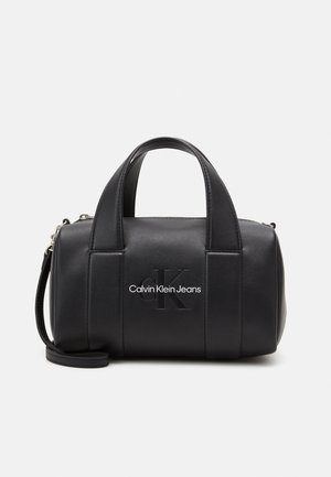 Czarna cylindryczna torebka Calvin Klein Jeans z podwójnymi uchwytami, odpinanym paskiem na ramię i wypukłym logo na przodzie.