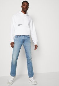 Hvit, cropped hettegenser med "Calvin Klein Jeans" logo, parret med lyse indigo rettbente jeans og hvite joggesko.