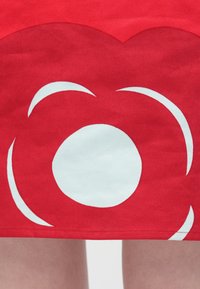 Červená látka má veľký biely kruhový vzor s zakrivenými akcentmi. Dizajn je výrazný, s hladkou textúrou a rovnomerným prešívaním na okraji.