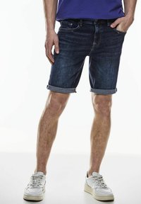 Pantalones cortos de denim en azul oscuro con dobladillos, que presentan un diseño clásico de cinco bolsillos y detalles de costura sutiles. Se llevan con zapatillas blancas.