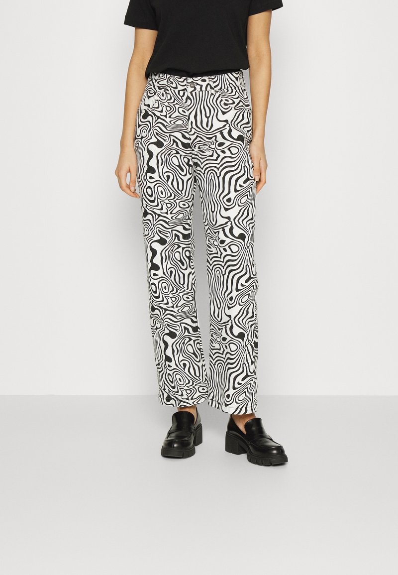 Pantalones de patrón en blanco y negro con una textura suave, cintura alta y diseño de pierna recta, combinados con zapatos negros gruesos.