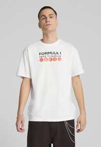 Hvid bomulds T-shirt med teksten "FORMULA 1 DRIVE TO SURVIVE" i sort og rød, korte ærmer og en afslappet pasform.