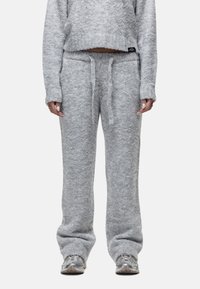 Persoon in zachte, lichtgrijze fuzzy breipantalons met een tailleband met trekkoord en een bijpassend lang mouwcroptop, gecombineerd met grijze sneakers.