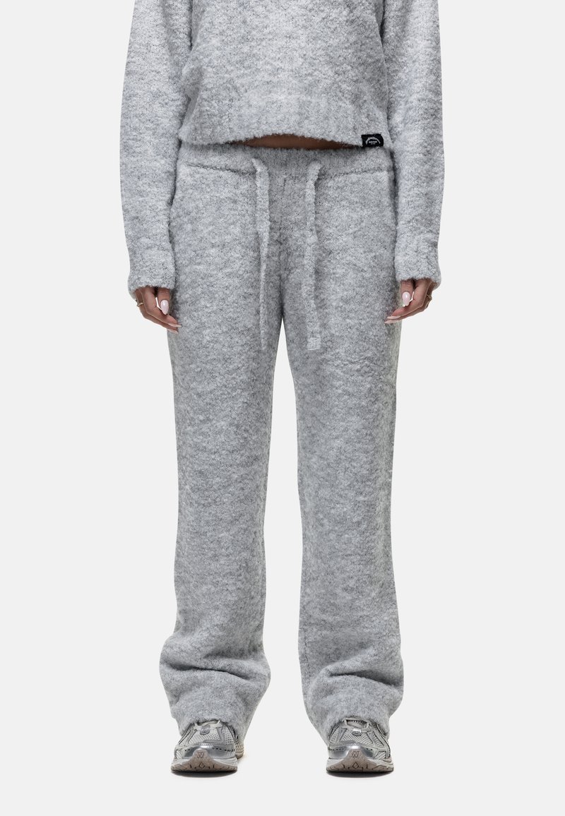 Persoon in zachte, lichtgrijze fuzzy breipantalons met een tailleband met trekkoord en een bijpassend lang mouwcroptop, gecombineerd met grijze sneakers.