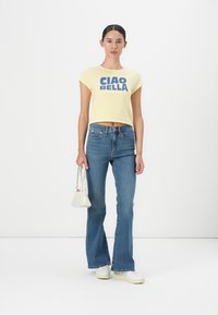 Yellow, cropped t-shirt with "CIAO BELLA" in dark blue letters; paired with light blue, flared jeans and white sneakers; small white handbag.