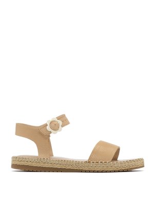 Sandale plate en cuir beige avec bride à la cheville ornée d'une boucle en forme de fleur blanche et semelle de style espadrille tissée.