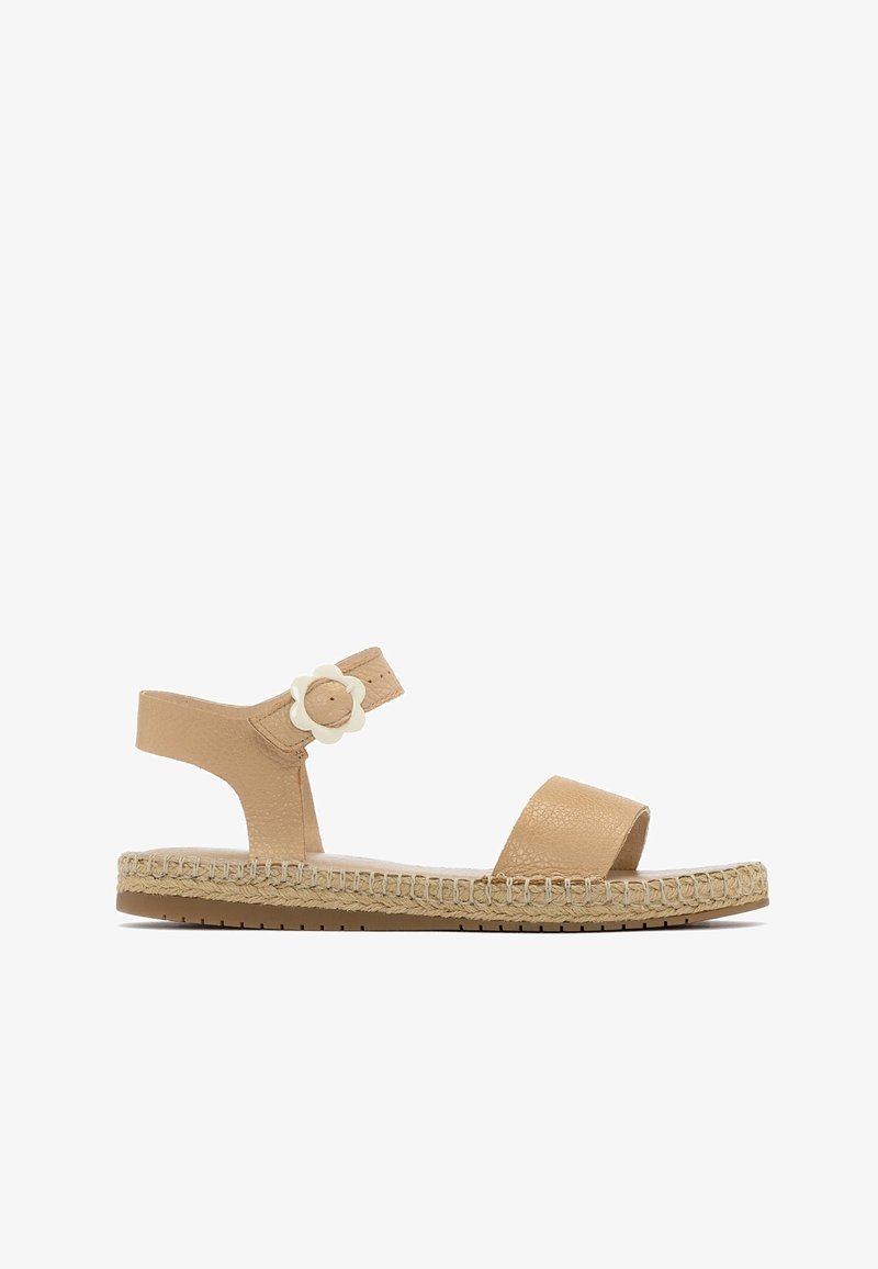Sandale plate en cuir beige avec bride à la cheville ornée d'une boucle en forme de fleur blanche et semelle de style espadrille tissée.