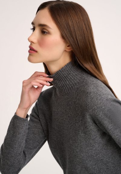 Grau gestrickter Pullover aus weichem, strukturiertem Material, mit einem gerippten Kragen und langen Ärmeln. Nahaufnahme des Profils eines Modells.