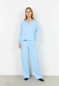 Conjunto de descanso azul claro que incluye una camiseta holgada de manga larga con escote en V y pantalones de pierna ancha con costuras verticales sutiles. Zapatos planos.