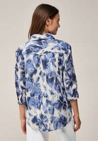 Camisa de patrón azul y blanco con cuello, mangas enrollables y un corte relajado. Textura suave y tejido ligero.