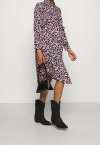 Černé květované šaty s dlouhými rukávy, růžovými a fialovými květinami, detaily kolem pasu; zkombinováno s černými kovbojskými botami a malou černou kabelkou.