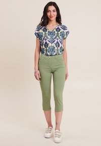 Top floreale a maniche corte con motivi blu e verdi, abbinato a pantaloni cropped verde chiaro e scarpe da ginnastica bianche. Tessuto liscio, vestibilità rilassata.
