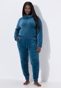 Teal fleece-loungevaatesetti, jossa on kauluskangas, tähtikuosi ja elastiset hihansuut. Jogger-housuissa on kiristysnauha vyötäröllä ja sivutaskut.