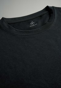 Čierne bavlnené tričko s okrúhlym výstrihom, s hladkou textúrou a minimalistickou etiketou s nápismi "THE SET" a "MADE IN BANJA LUKA."