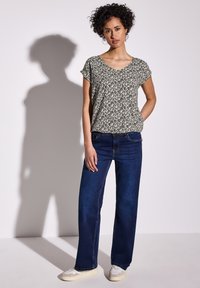 Top dal taglio rilassato in un colore crema chiaro con un motivo floreale nero, abbinato a jeans a gamba larga blu scuro e sneakers beige.