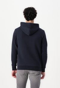 Navyblauwe hoodie van zacht materiaal, met een trekkoordcapuchon, ribgebreide manchetten en een ontspannen pasvorm. Grijze jeans eronder zichtbaar.