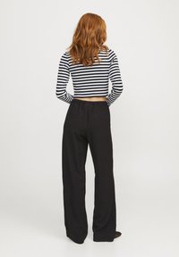 Svart vide bukser med teksturert stoff, parret med en svart og hvit stripet cropped topp. Toppene har lange ermer og en tettsittende design.