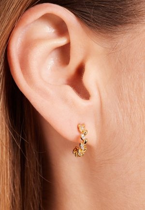 Boucles d'oreilles en or en forme de hoops avec des maillons en forme de cœur ornés de pierres claires, offrant une finition lisse et polie au contact de la peau.