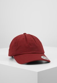 Cappellino da baseball in cotone rosso con visiera curva, sei pannelli e bottone superiore. Presenta un'etichetta con il marchio sul lato. Texture liscia.