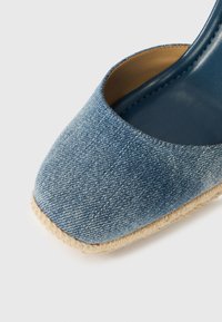 Παπούτσι espadrille από τζιν με τετράγωνη μύτη, επάνω μέρος από ανοιχτό μπλε ύφασμα και σόλα τυλιγμένη με τζούτ. Το εσωτερικό έχει επένδυση από λείο μπλε υλικό.