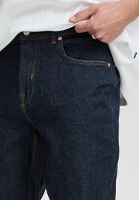 Dark denim jeans with yellow stitching, five-pocket design, and a straight fit. Material appears sturdy with a smooth texture.