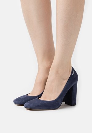 Escarpins en suede bleu marine à talons hauts avec un bout arrondi et un talon bloc. Marque discrète sur le talon, texture lisse et design épuré.