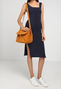 Robe midi rayée bleu marine avec un col en U, fente latérale ; associée à un sac à main en daim moutarde et des baskets blanches.