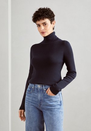 Marineblau gerippter Rollkragenpullover mit tailliertem Schnitt, langen Ärmeln und glatter Textur, kombiniert mit hellblauen, hoch taillierten Jeans.