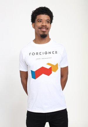 White cotton t-shirt featuring black text "FOREIGNER AGENT PROVOCATEUR" and a colorful geometric design in red, blue, and yellow.