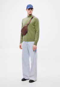 Olívazöld kötött pulóver, világoskék bő szárú farmer, barna keresztpántos táska és kék sapka, modern laza stílust bemutatva.