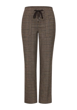 Persoon draagt bruine geruite broek met een zwart trekkoord en een bordeauxrode blouse, met één hand in de zak en de andere ontspannen naast het lichaam.