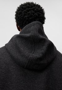 Felpa con cappuccio grigia scura realizzata in morbido tessuto, caratterizzata da una superficie testurizzata e un dettaglio con logo ricamato lungo il bordo del cappuccio.