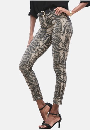 Schlanke Hosen im beigefarbenen und schwarzen Tigerprint. Aus strukturiertem Stoff mit sichtbaren Nähten, getragen mit einem schwarzen Gürtel und hohen Sandalen.