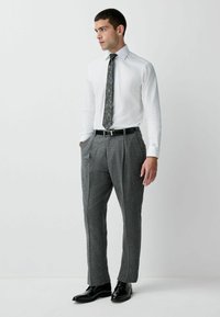 Valkoinen kauluspaita, kuviollinen solmio, harmaat ruudulliset housut, joissa on laskokset, ja mustat siistit kengät. Siisti muotoilu perinteisillä ompelutiedoilla.