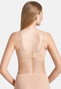 Beige bra with adjustable straps, seamless design, and a hook closure at the back. Made from soft, stretchy fabric. Smooth texture.