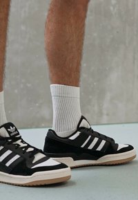 Zwart-witte sneakers van suede en mesh materialen, met drie witte strepen, een rubberen zool en een gestructureerd design.