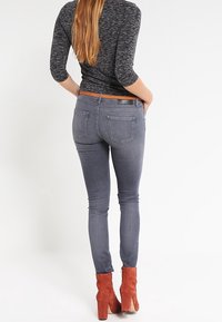 Dünne graue Jeans mit mittelhohem Bund, die über orangefarbenen Wildlederschnürstiefeln sitzt. Verfügt über normale Gesäßtaschen und eine strukturierte Oberseite.